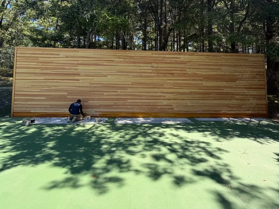 Hyannis Painting painter kneeling at a cedar wall while applying wood stain