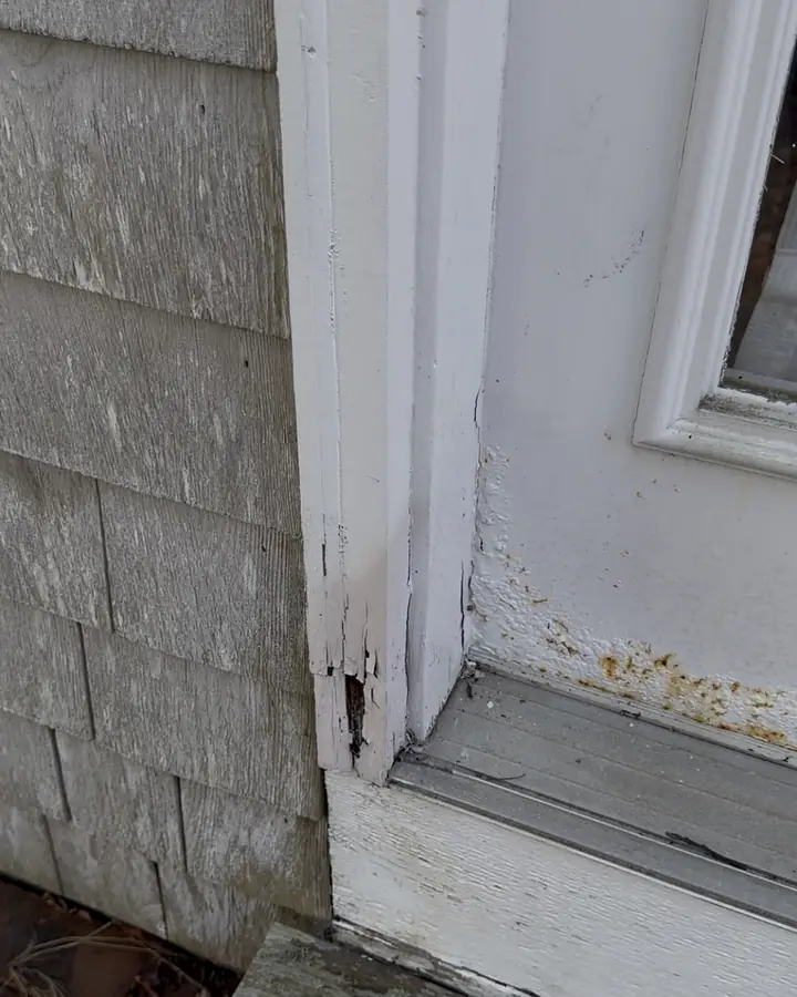 White door trim rotted and split at the bottom, next to weathered cedar shingles and a door sill